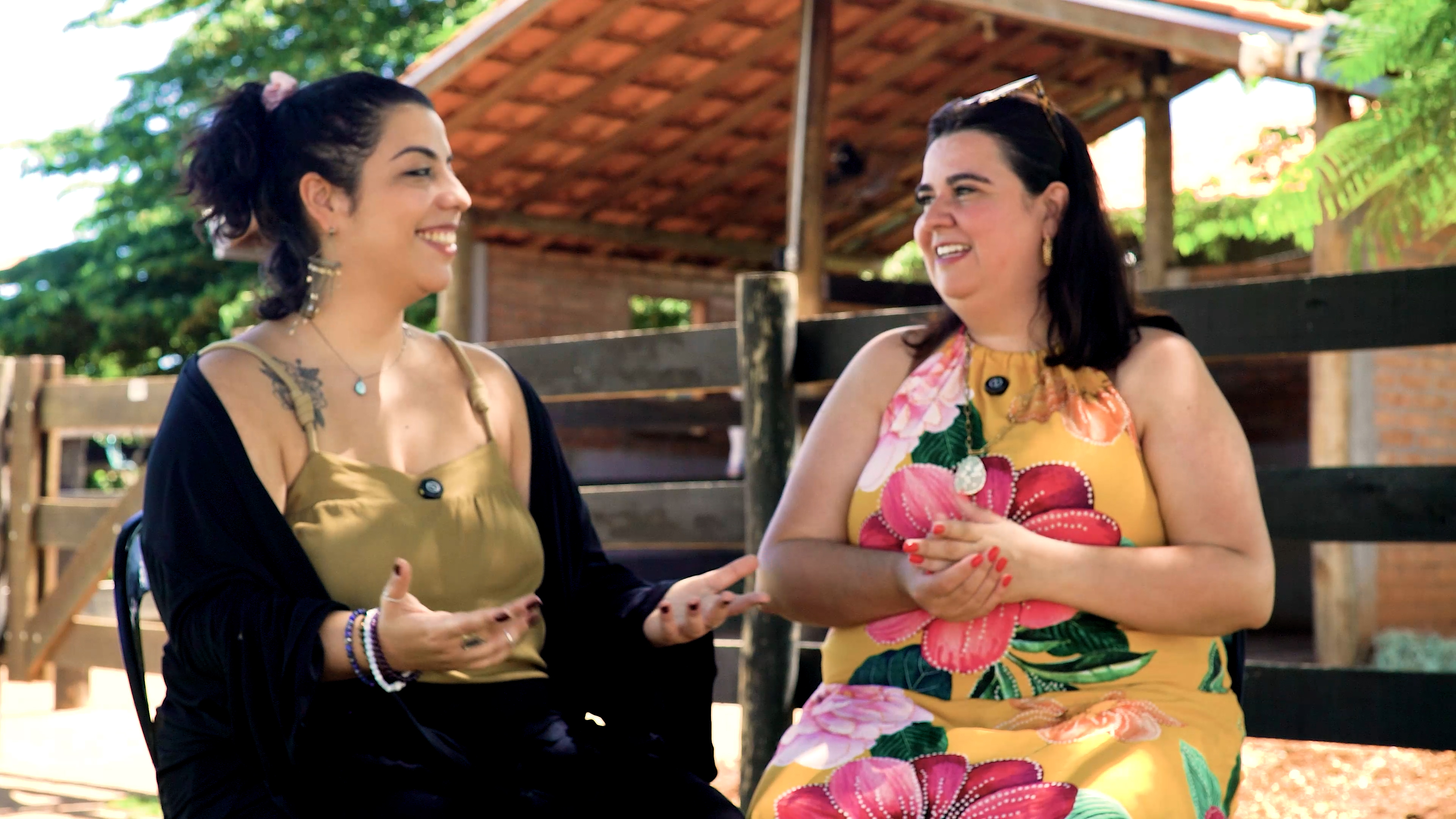 Heloísa de vestido floral e uma convidada sorrindo e conversando em ambiente rural